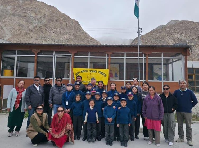 The monitoring team, teachers and students gathered in front of a school building beneath the national flag
