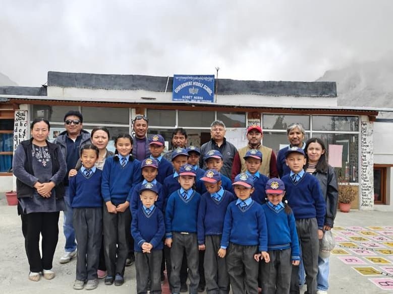 The monitoring team with students in blue uniforms and staff in a school courtyard under a cloudy sky
