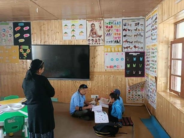 A teacher with young students at work in a wood-panelled classroom lined with learning charts