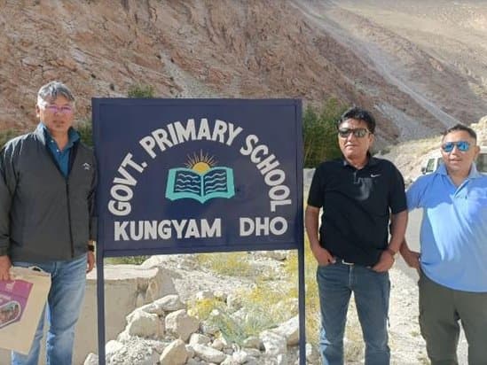 Three members of the monitoring team beside the signboard of Govt. Primary School, Kungyam Dho
