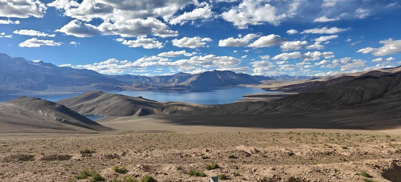 A high-altitude lake in a wide, open valley of the Changthang plateau under scattered clouds