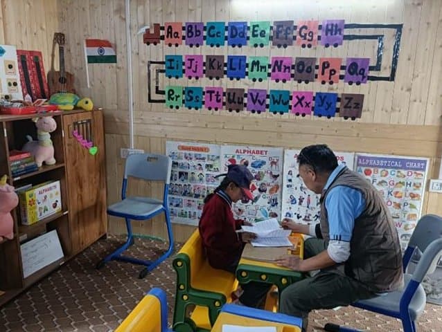 A member of the monitoring team reviewing a student's work at a small table in a brightly decorated primary classroom