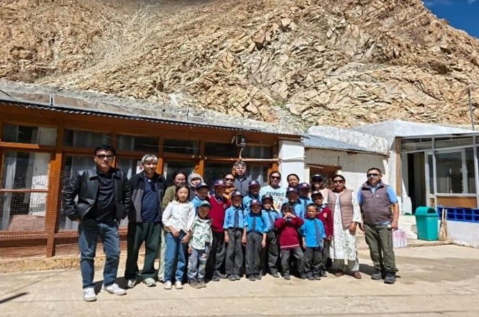 The monitoring team with students and teachers outside a school building at the foot of a rocky mountainside
