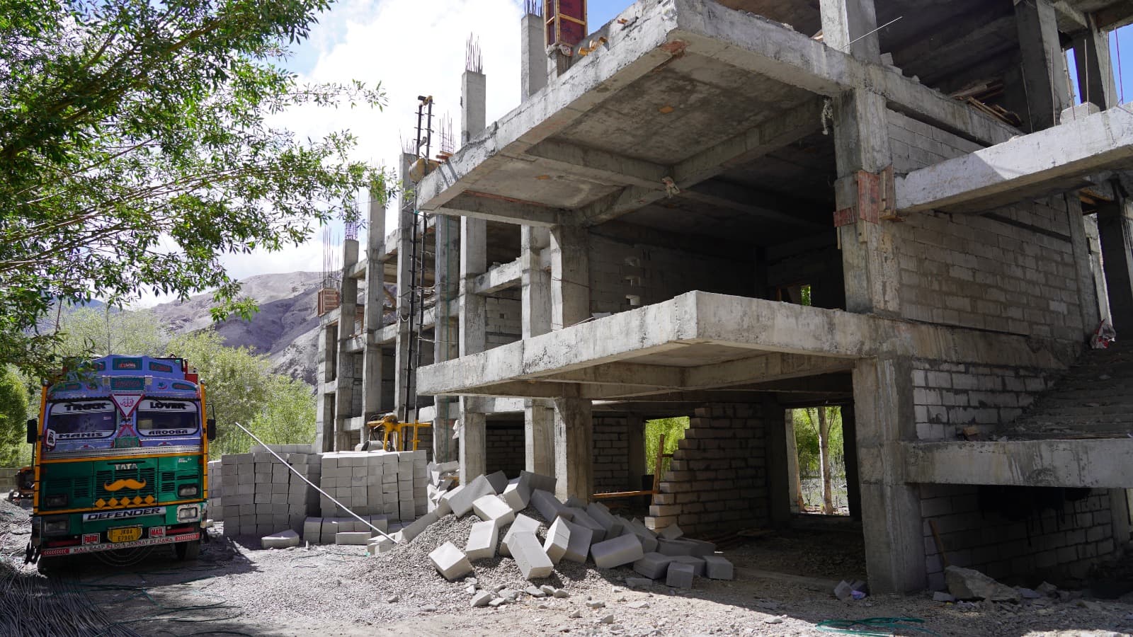 A new multi-storey school building under construction in the Lingshed–Fotoksar belt, with a truck and stacked blocks in the foreground