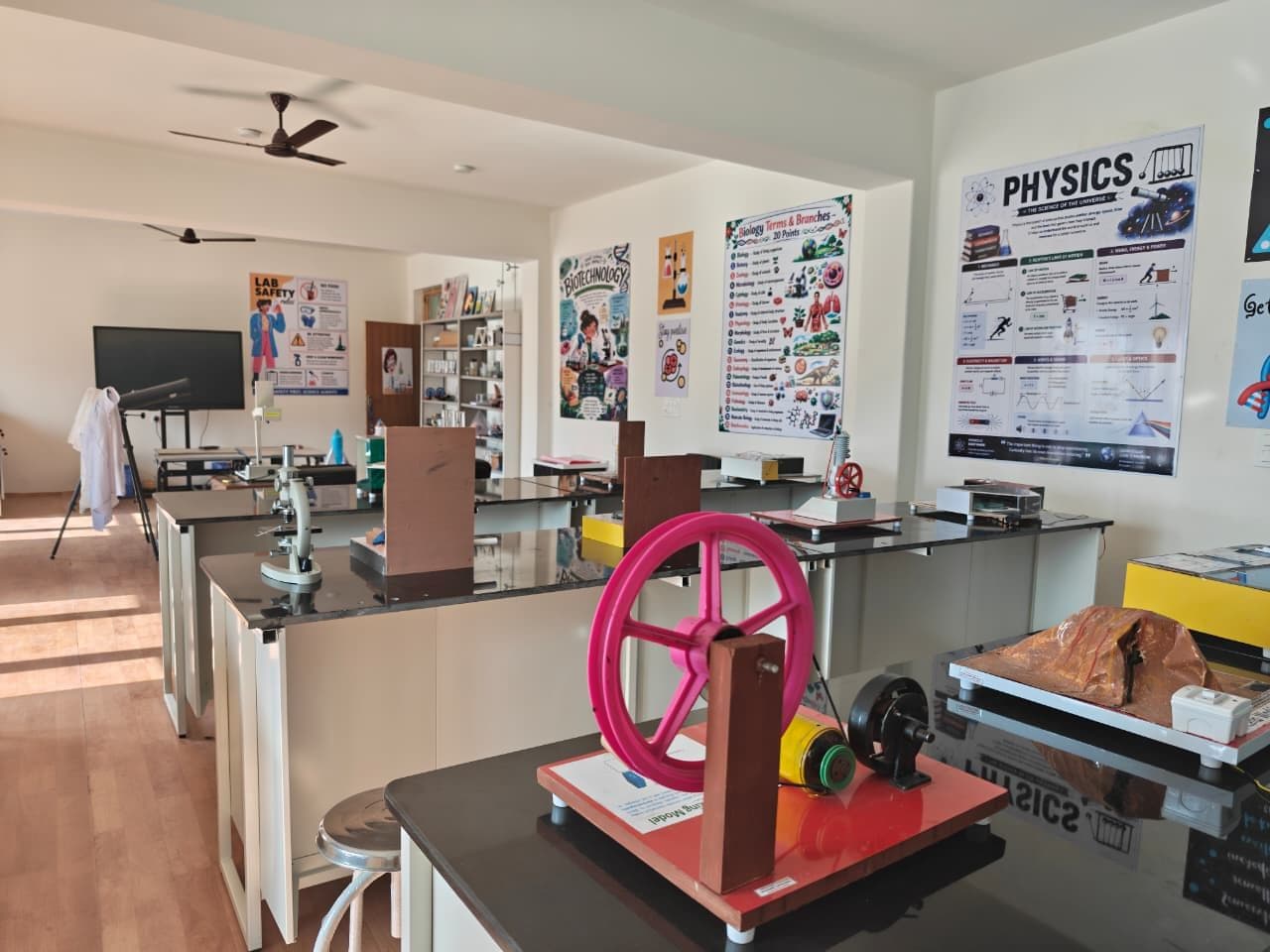Working science models on black-topped lab benches, with a telescope, a smart TV and science posters behind
