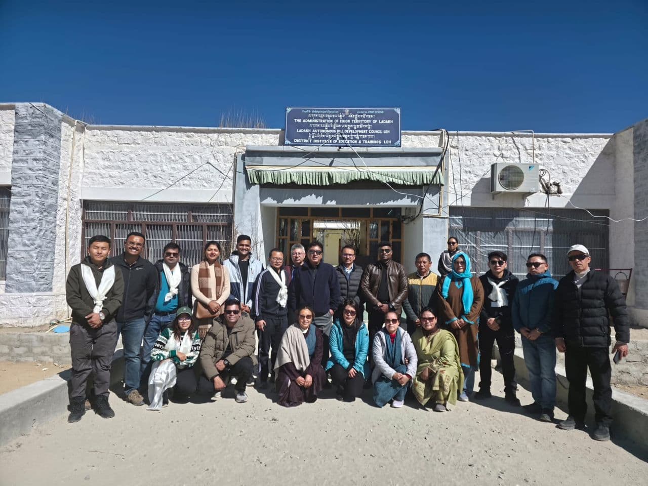A batch of IAS officers with DIET Leh faculty, standing in front of the DIET Leh building under a clear blue sky
